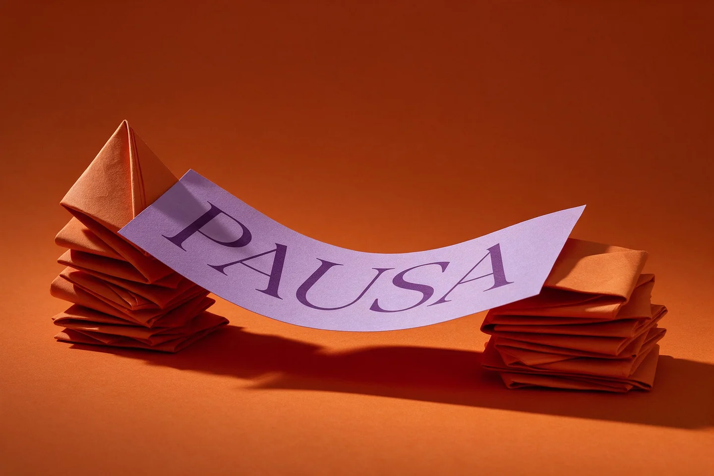 Uma faixa de papel lavanda com a palavra “Pausa” forma uma curva suspensa entre pilhas de papel.
